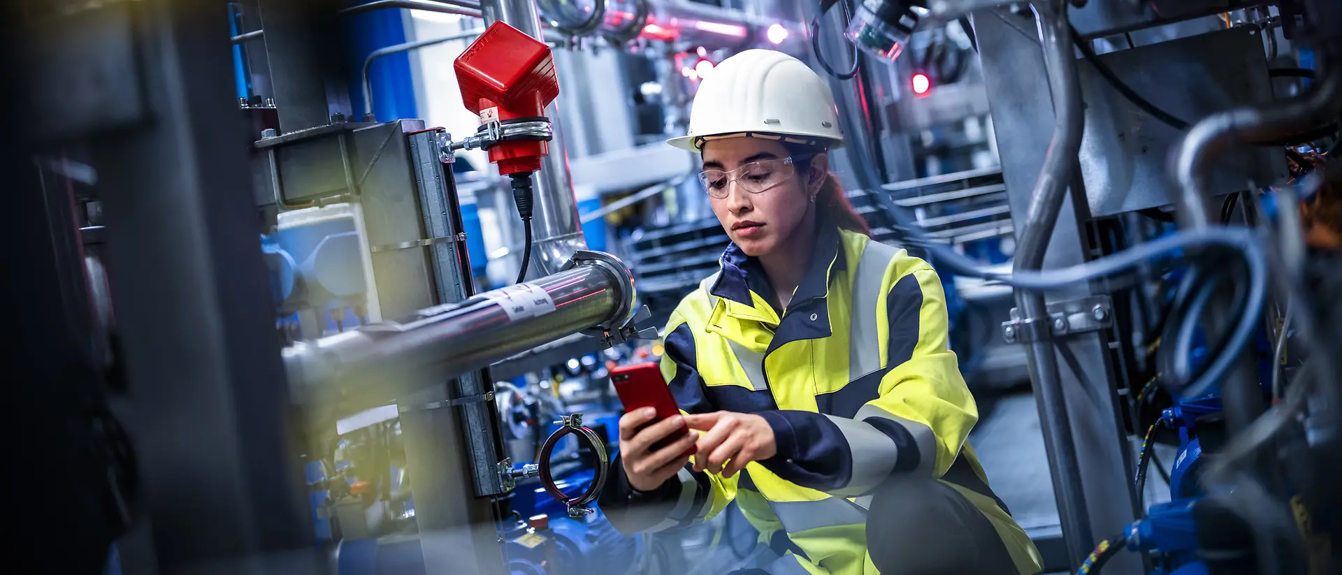 A female worker is standing in a production site checking on her mobile device the status of the equipment.