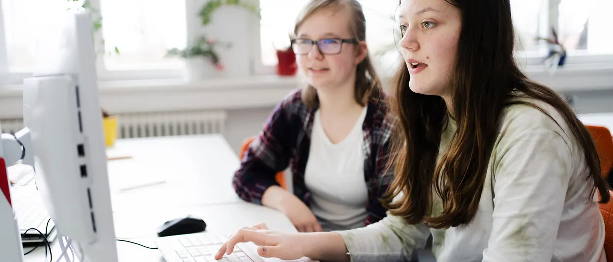 A college graduate helps a school student on a computer