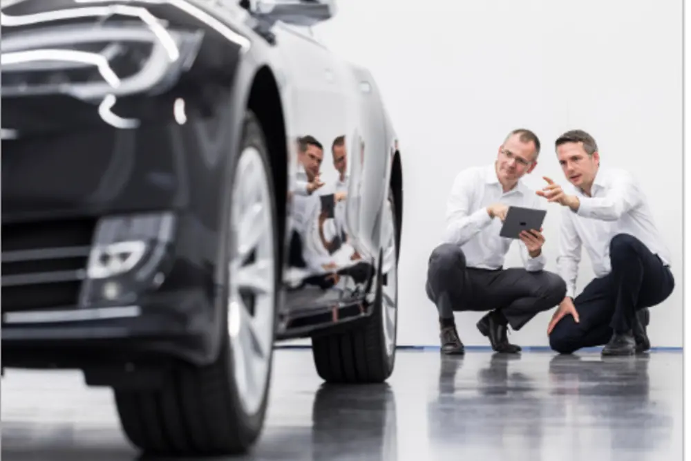 Two Henkel employees standing discussing behind a car.