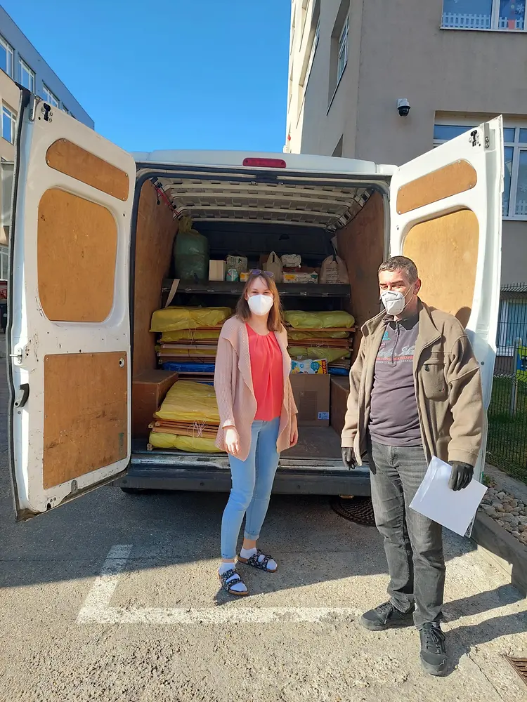 A woman and a man standing in front of a van loaded with cribs and mattresses that are being donated.