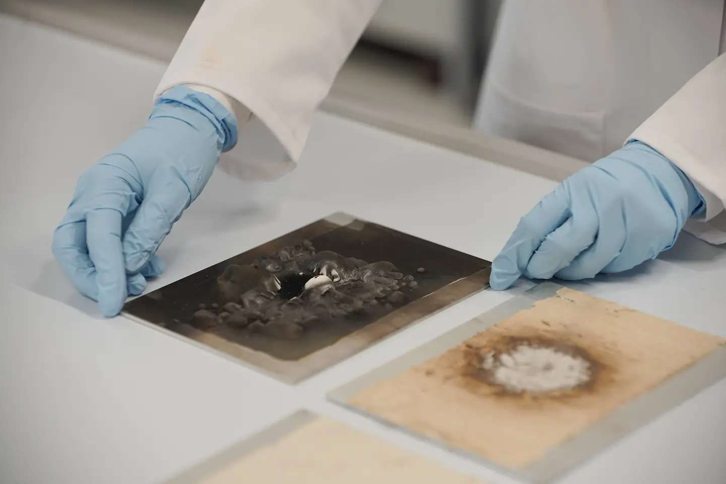 Lab technician examining the results of an open flame test on 2 metal sheets, one coated with Loctice EA 9400, whereas the other is coated with Loctite FPC 5060.