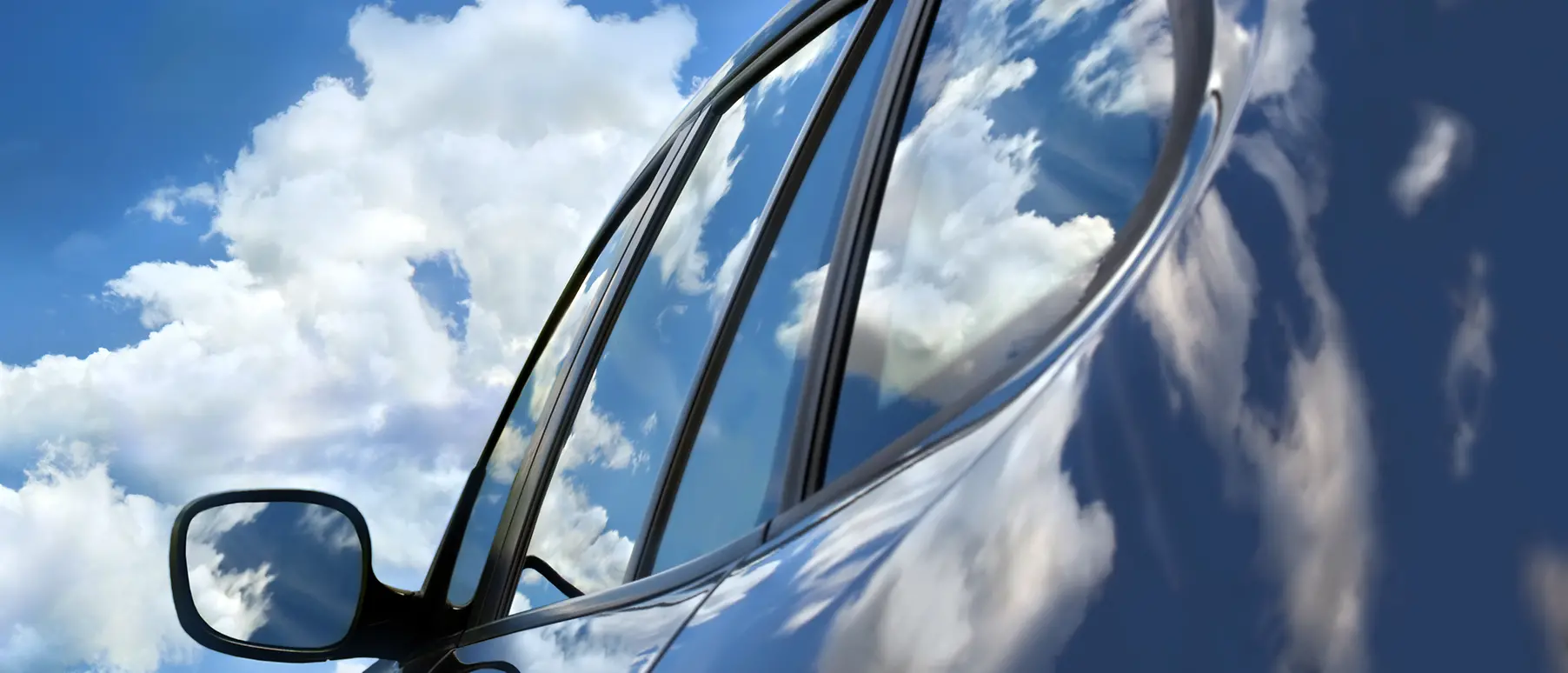 A car with sky and clouds reflecting on surface