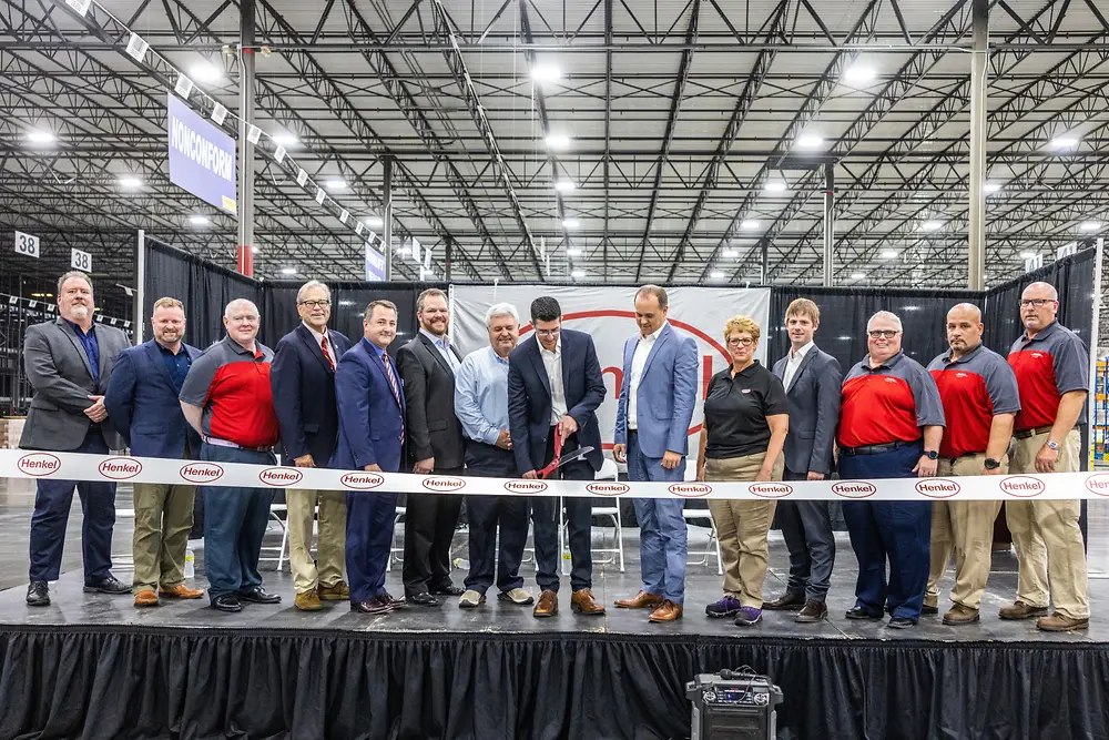 14 people standing behind a Henkel-branded ribbon, watching it being cut