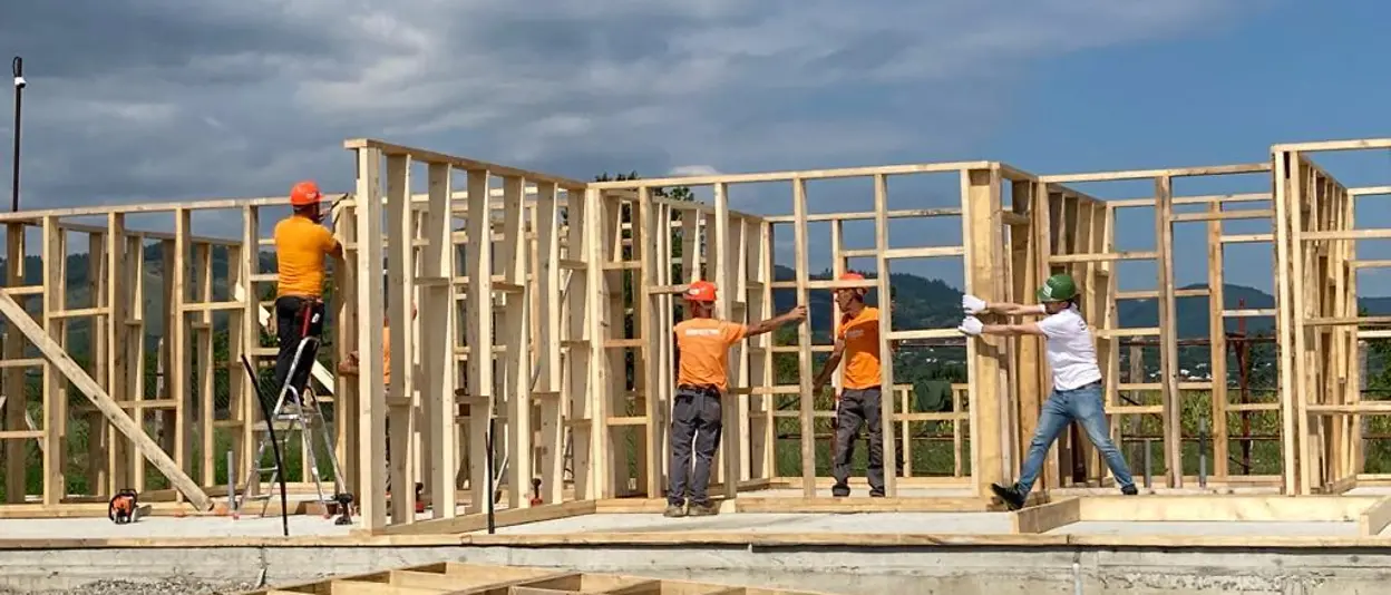 Four helpers work on the wooden frame of the house.