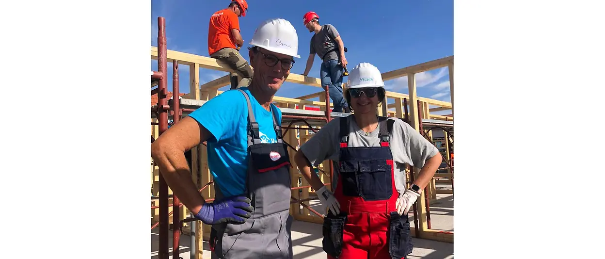 Henkel employee Bernd stands together with another helper in front of the wooden frame of the house.