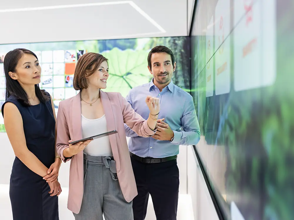 A customer experience tour guide showing two customers interactive content in the Infinity Room of the Inspiration Center Düsseldorf.