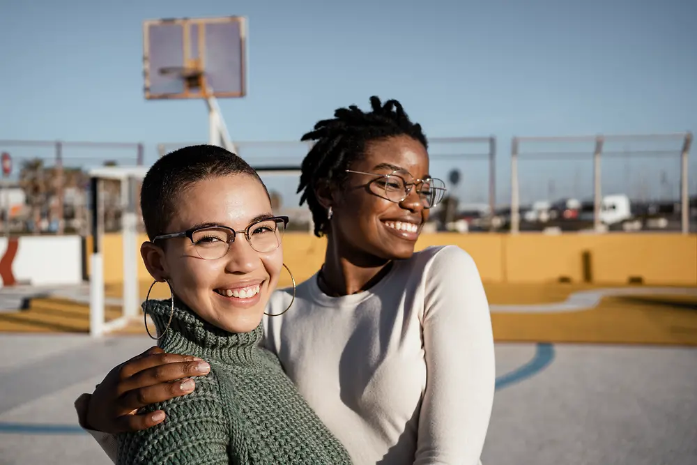 Two women standing laughing and hugging on a basketball court.