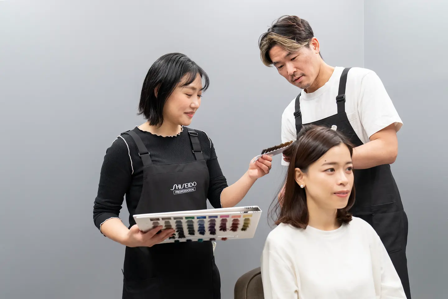 Two evaluators examine the hair of a woman. 