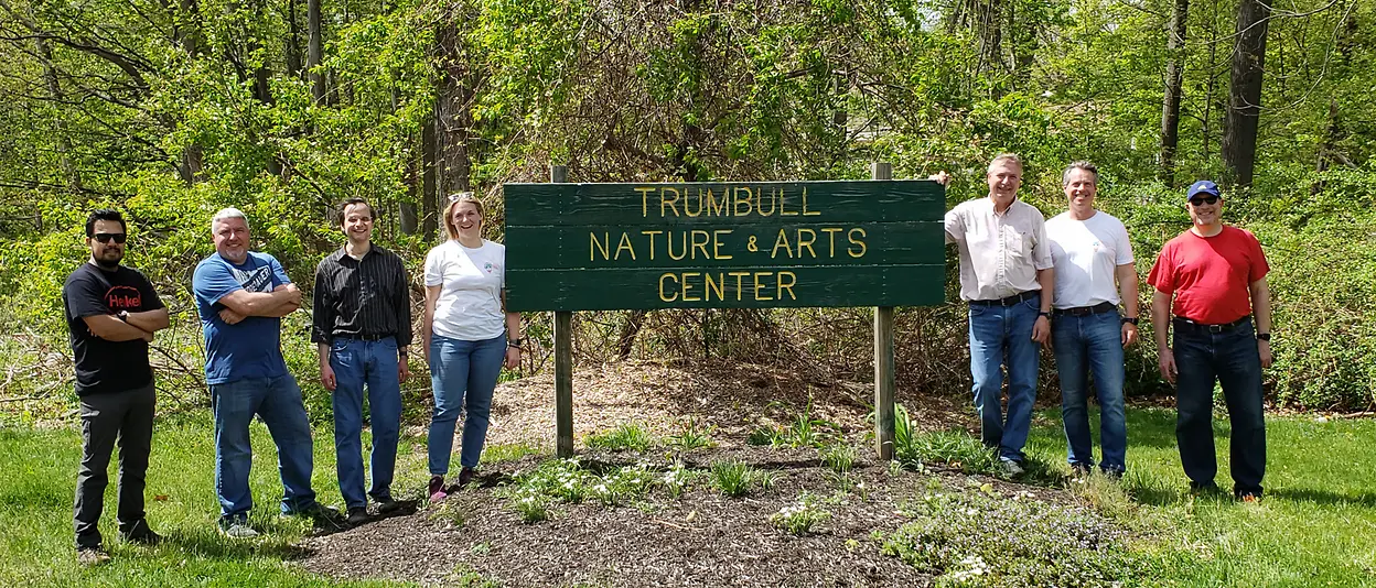 Henkel employees work on cleaning up a yard, with rakes and a wheelbarrow.