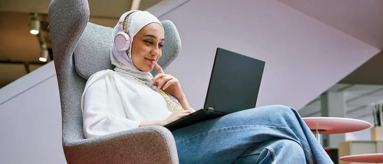 An employee sits in an armchair and looks at the screen of her laptop.