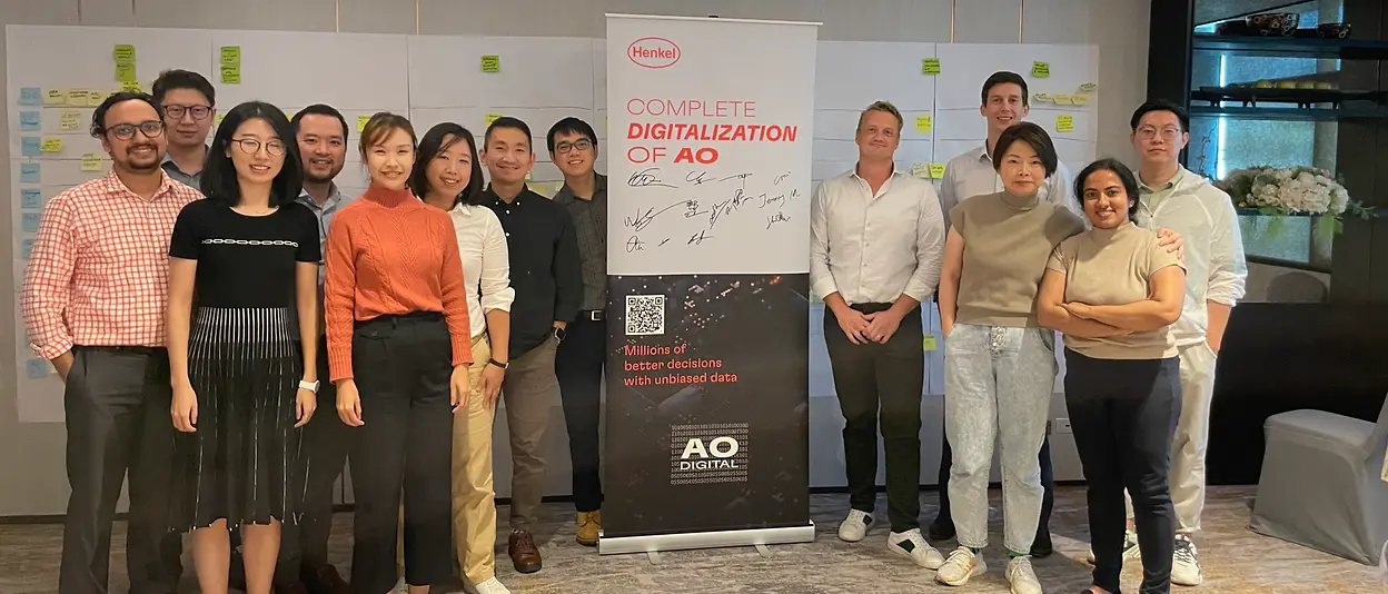 Nick and his team stand together in a meeting room posing next to a roll-up that says “Complete Digitalization of AO”.