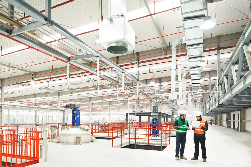 Two people stand in an Adhesive Technologies production site looking at digital devices in their hands.