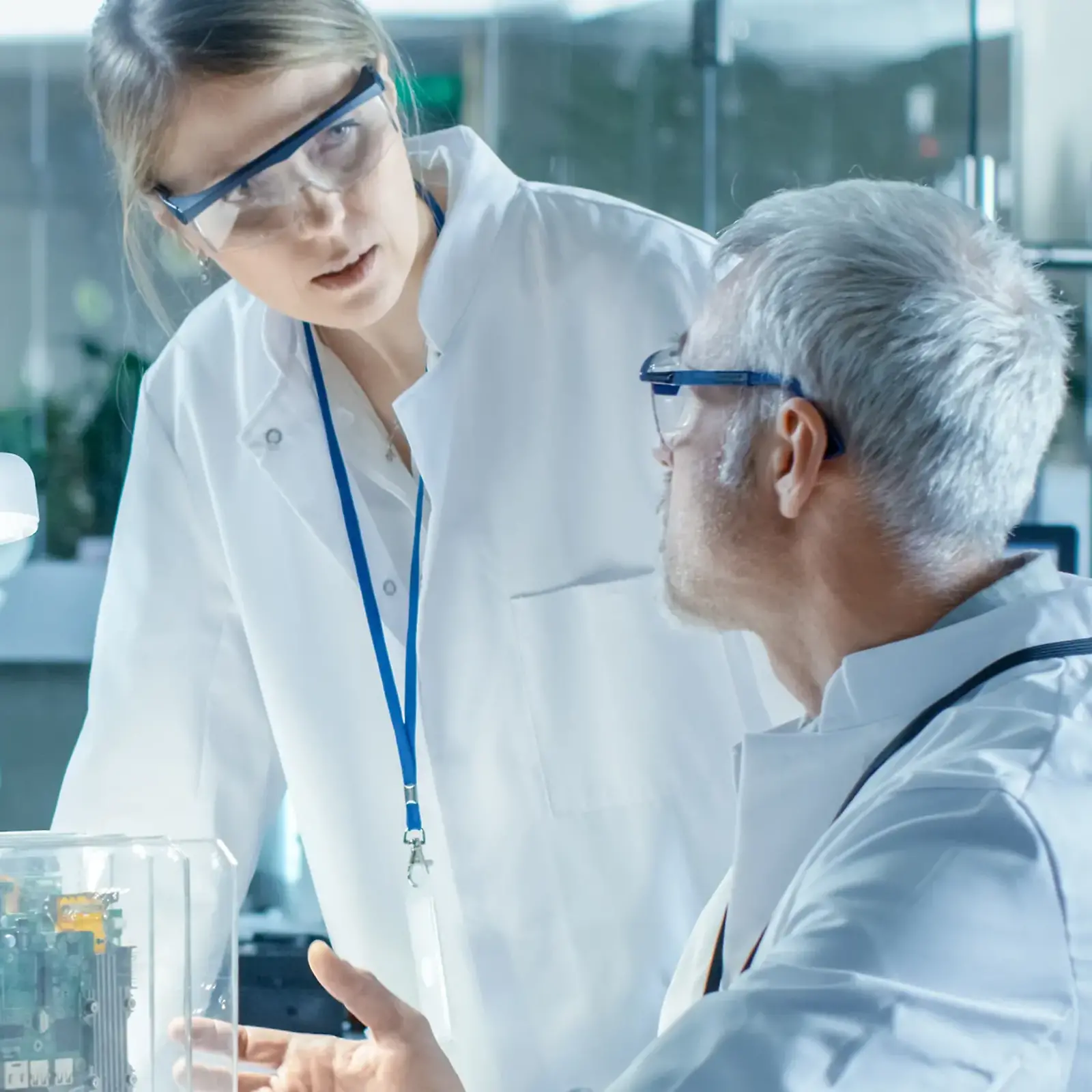 Two laboratory employees in lab coats talk and discuss about the experimental work in front of them.