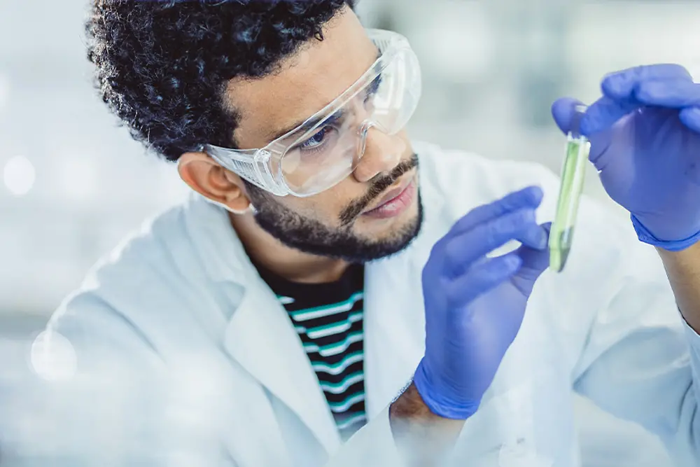 Young researcher in a lab holds and observes a test tube.