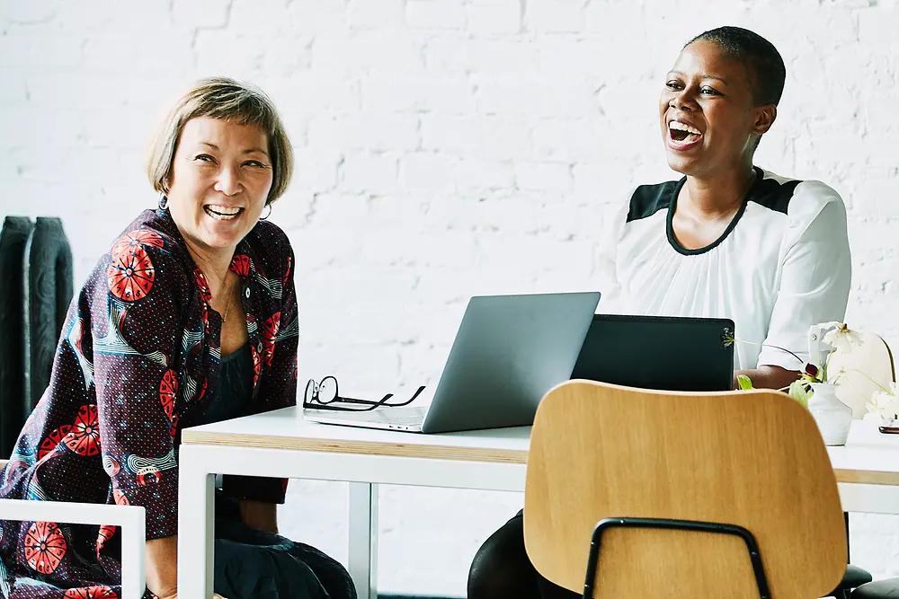 Two women of different ages are talking and laughing in the office.