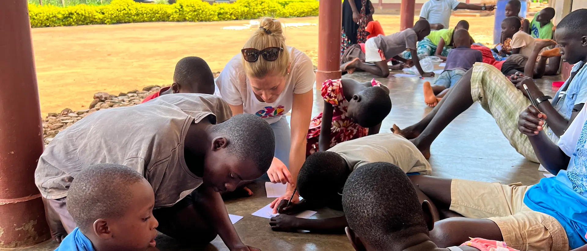 The volunteers and children sit on the floor and paint.