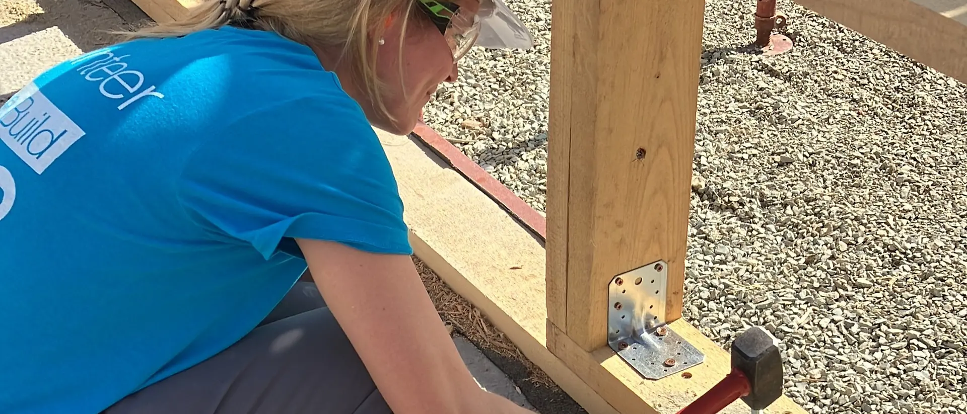 A volunteer uses a hammer on a building site.