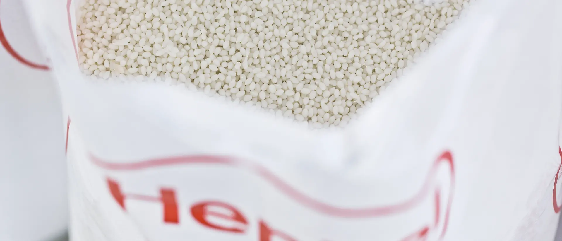 Close-up of a white, Henkel-branded bag containing white pellets.