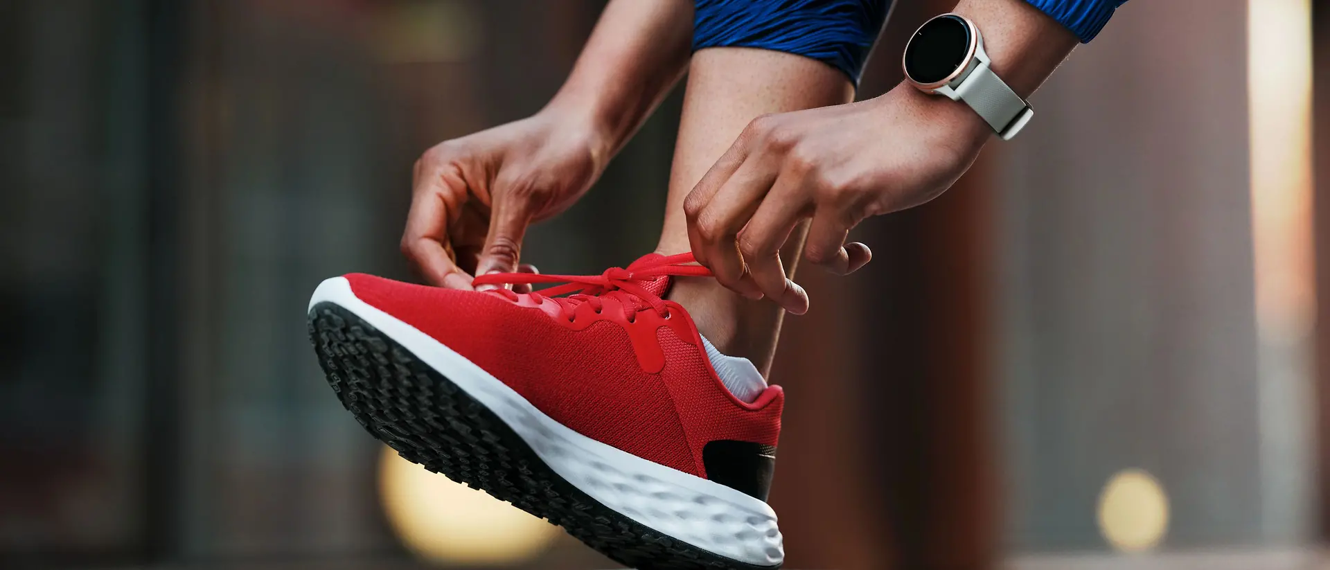 A person lacing up sports shoes bonded with solutions from Henkel Adhesive Technologies and wearing a smartwatch.