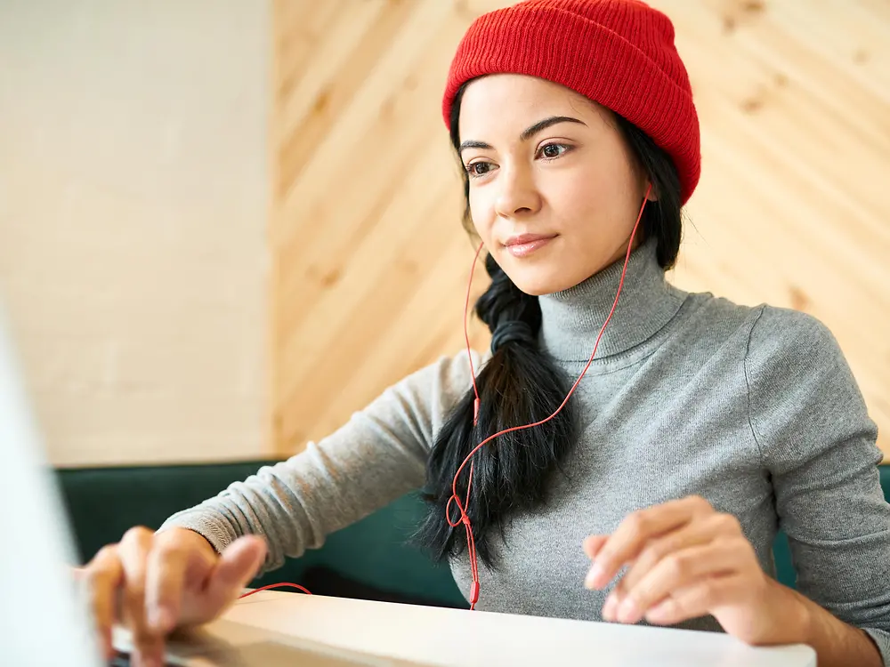 Young woman wearing a red beanie hat using laptop whileusing laptop