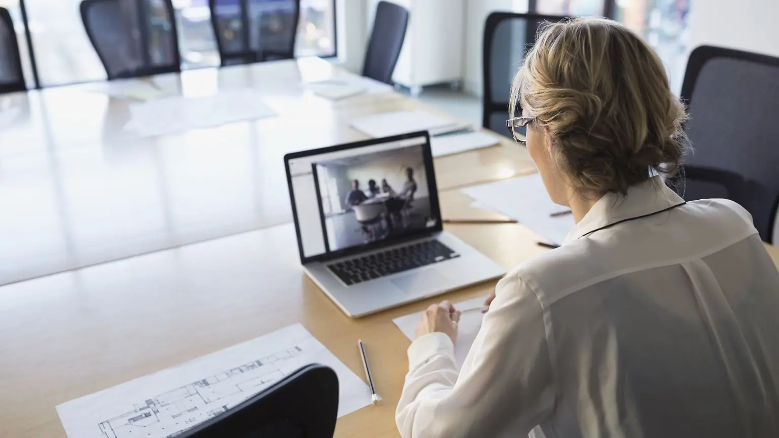 A woman sitting in a boardroom table watching a video on a laptop.