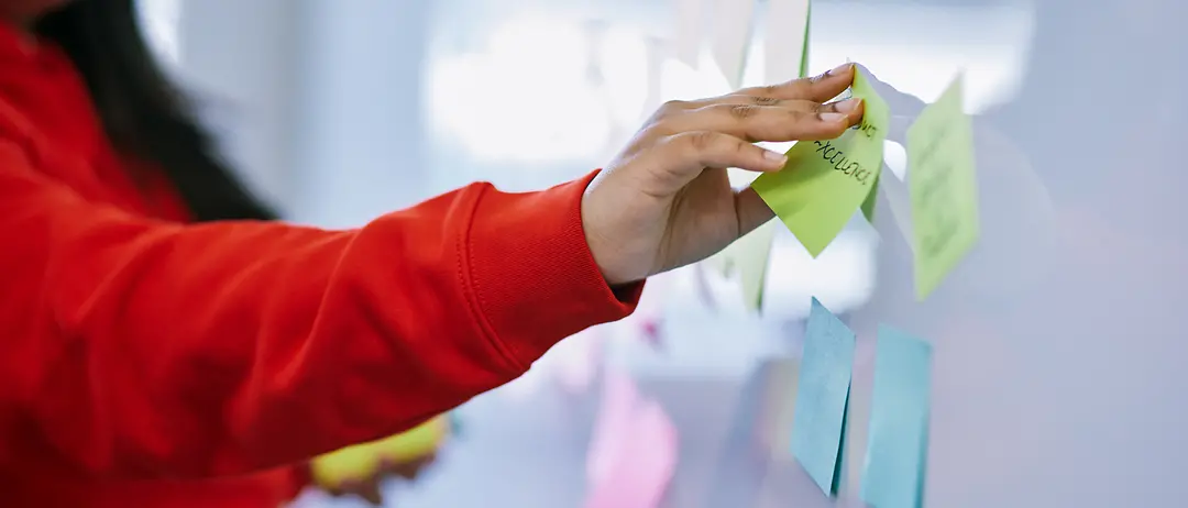 Eine Frau in einem roten Pullover klebt Post-Its an ein Whiteboard