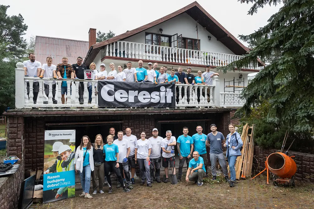 The 'Build for a Good Cause' and the Polish Ceresit team from Henkel stand in front of the house they are renovating together and smile at the camera.