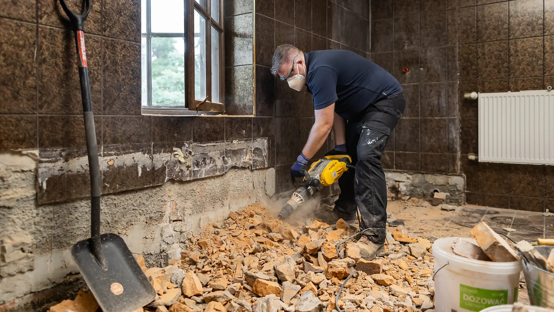 A man in protective clothing carefully removes tiles with a hammer drill.