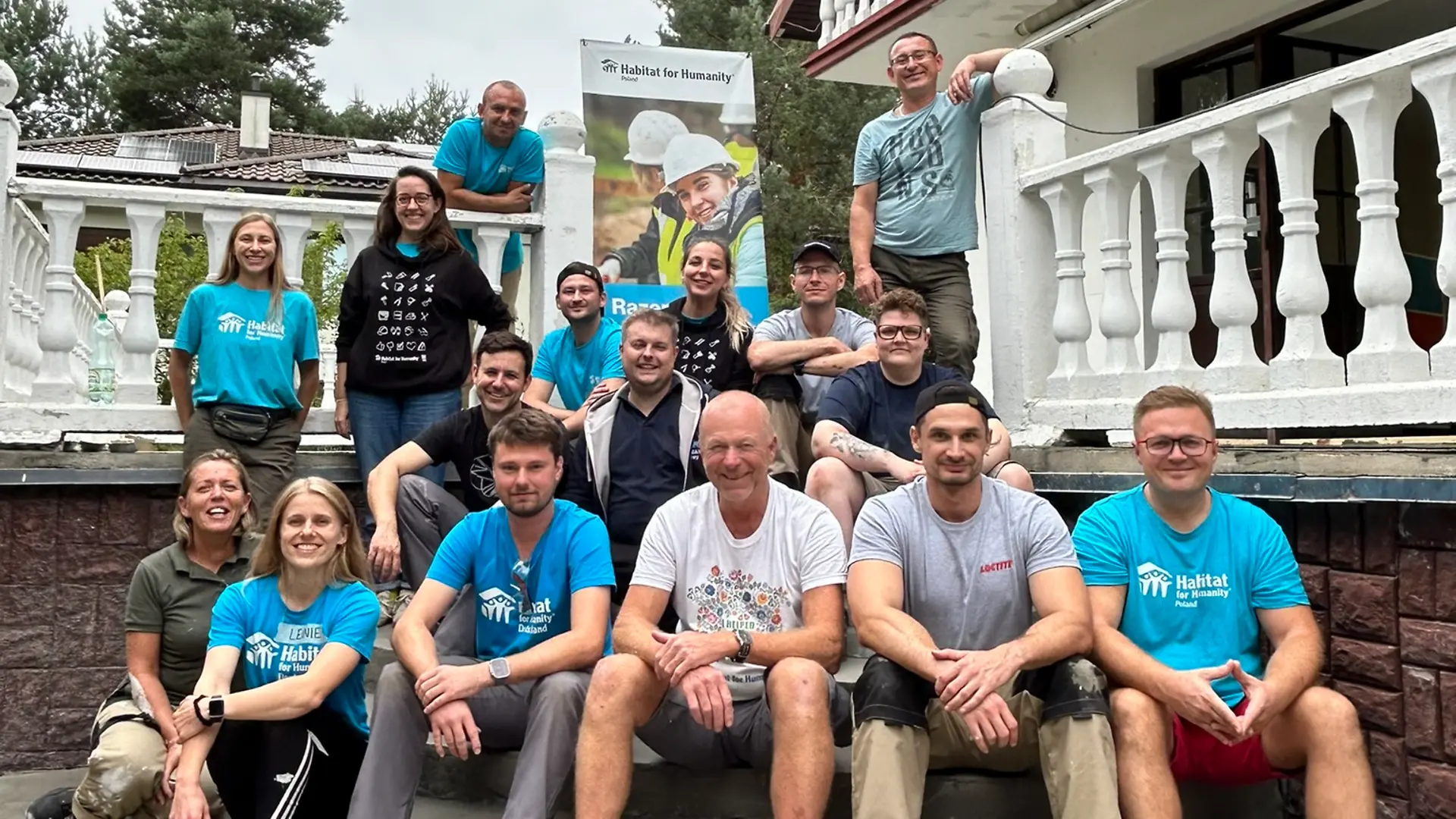 The ‘Build for a Good Cause’ team sits on a flight of steps in the garden of the house and smiles into the camera.