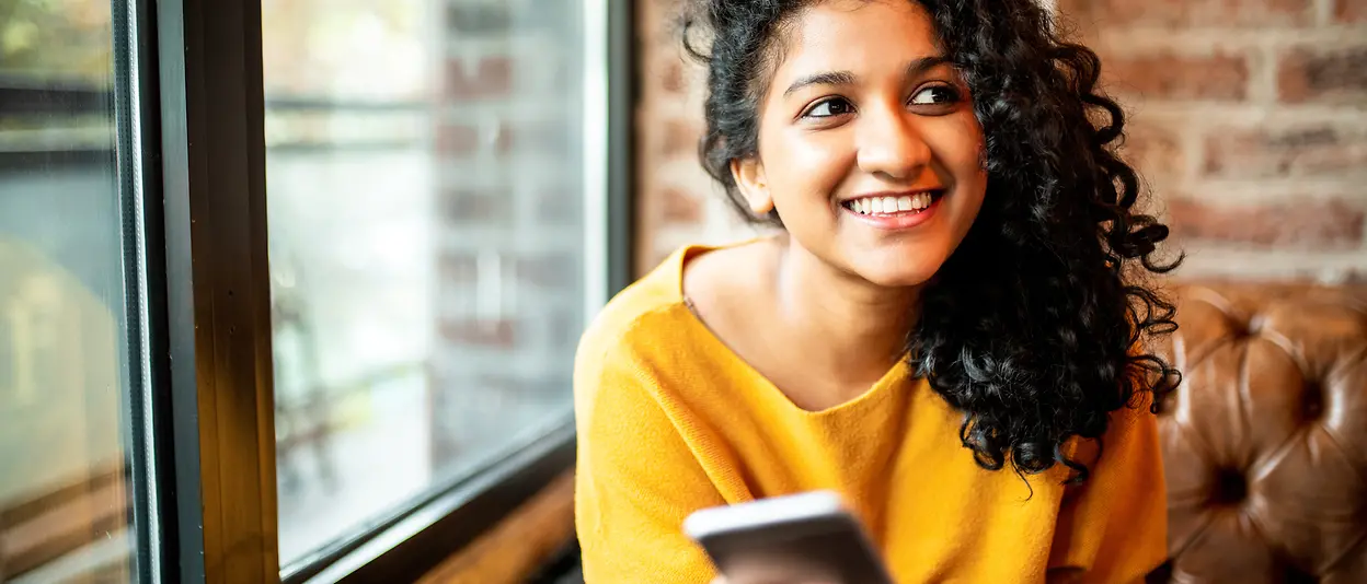 A woman is holding a smartphone in her hand while smiling.