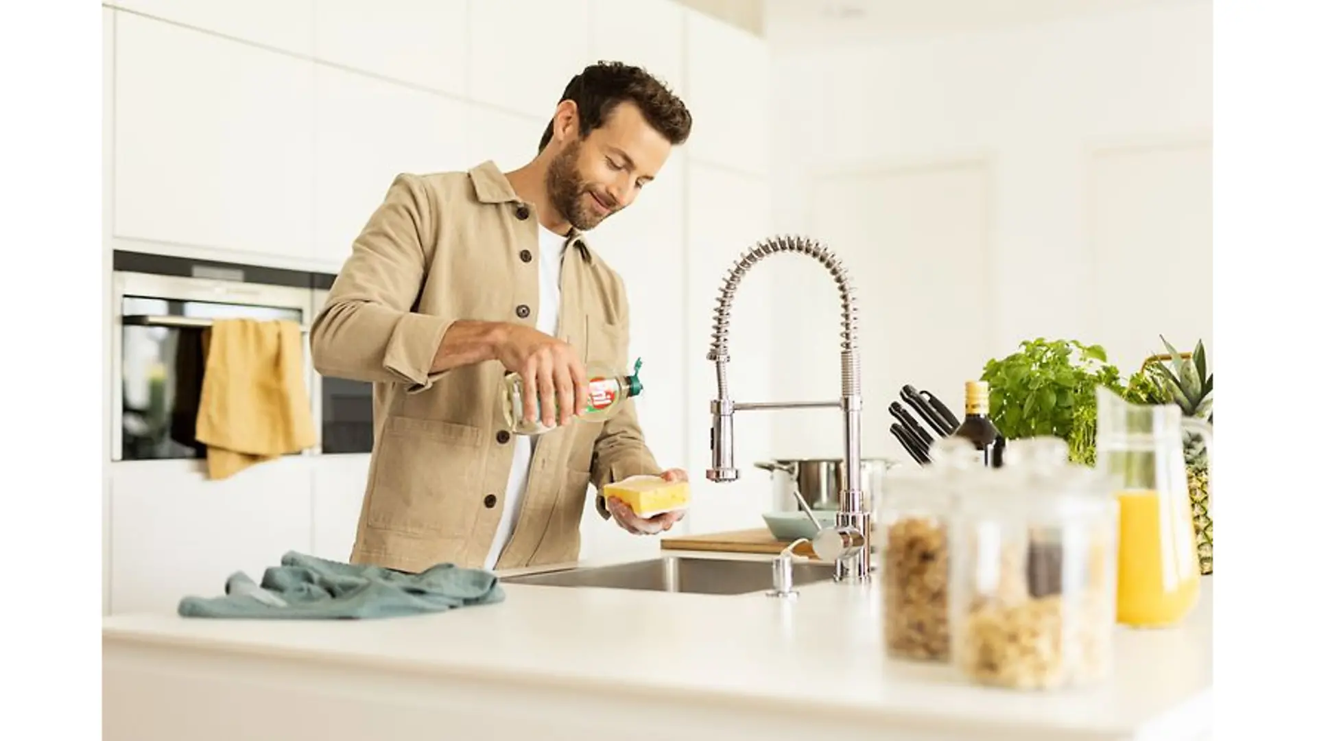 Man stands at the sink and pours Pril onto a sponge.